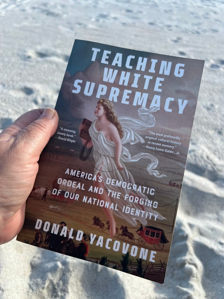 Hand holding a book with a sandy beach backdrop