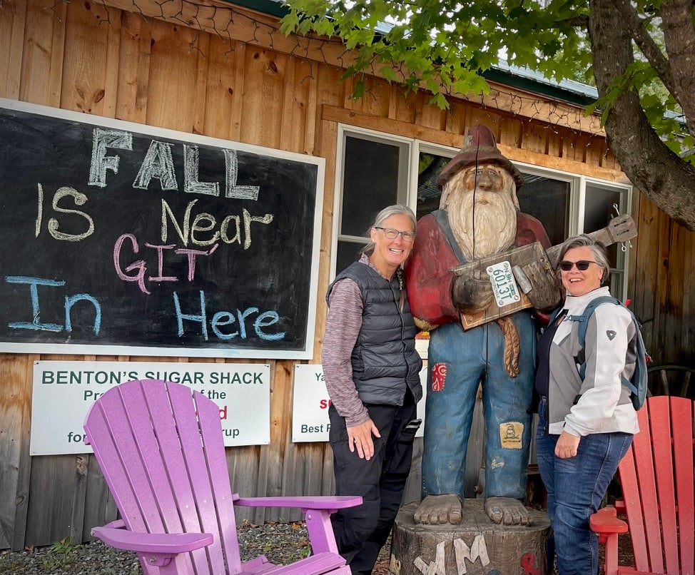 two motorcycle babes with a wood cut statue of a mountain man 